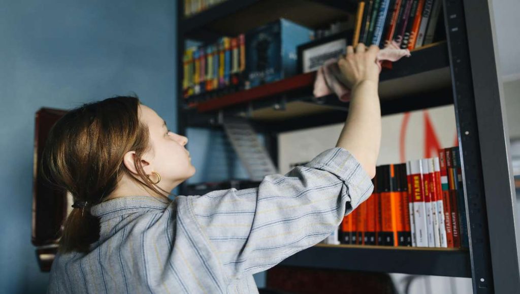 Woman wiping and cleaning the bookcase